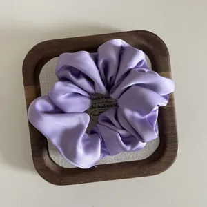 Detailed view of a light purple satin scrunchie on a rustic wooden display tray