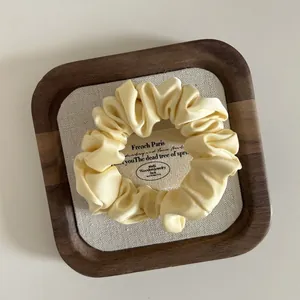 Close-up of a pale yellow satin scrunchie with soft silk texture on a wooden tray