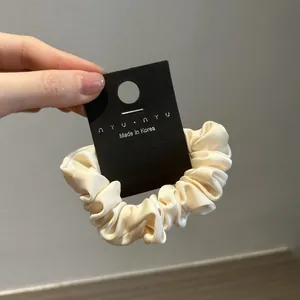Dettaglio dell'elastico in raso crema con trama plissettata setosa su carta