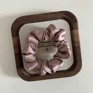 Detailed close-up of silky mauve satin scrunchie with soft folds on wooden tray