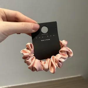 Dettaglio di un elastico per capelli in raso rosa con texture a pieghe morbide