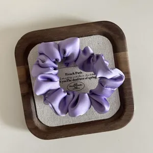 Detail shot of a lilac satin scrunchie resting on a vintage wooden display tray