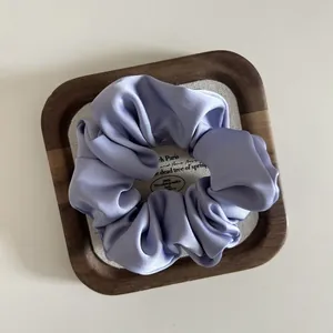 Close-up of lavender satin scrunchie with glossy texture on a wooden jewelry tray