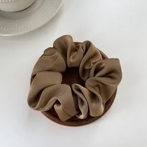 Detailed view of coffee brown satin scrunchie with soft sheen on a wooden display stand