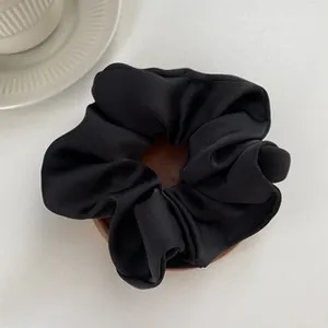 Close-up of black satin hair scrunchie with smooth silk texture on white background