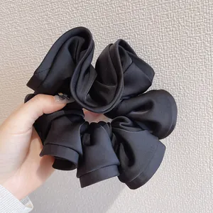Détail d'un chouchou en satin noir multicouche avec un accent doré tenu à la main