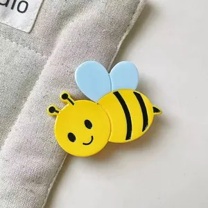 Pince à cheveux abeille avec corps jaune et ailes bleues sur fond de tissu gris clair