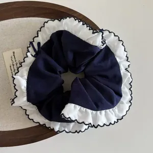 Detail of navy blue oversized scrunchie with white ruffle trim on a wooden tray