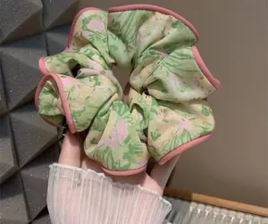 Detail of green floral oversized scrunchie with pink edges held in hand close-up