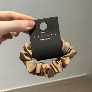 Dettaglio di scrunchie in raso color oro champagne con consistenza setosa su carta