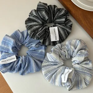 Trois chouchous en tissu à rayures noires, marine et bleues sur un fond aux tons doux