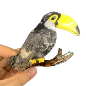 Handheld toucan-shaped acetate shark hair claw clip with yellow beak and marble pattern