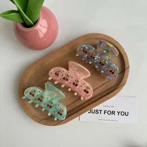 Détails de trois pinces à cheveux cerise en acétate avec strass sur plateau bois