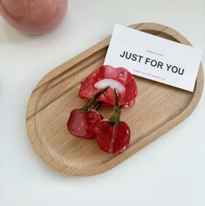 Détail d'une pince à cheveux cerise rouge translucide avec feuille verte sur bois