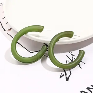 Detail of olive green matte acrylic C-shaped earrings with fine metal needles on white plate