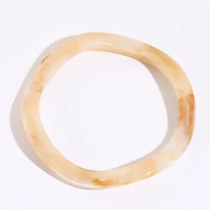 Dettaglio di un bracciale a torsione in resina con trama marmorizzata ambra su bianco
