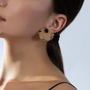 Acetate shell-shaped earrings with tortoiseshell pattern on a model side profile