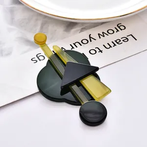Modern geometric acrylic brooch with green elements on a white ceramic plate background