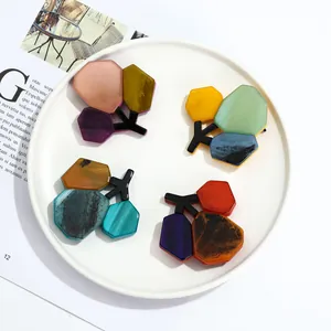 Detailed macro of colorful acrylic branch brooches with marble texture on white ceramic