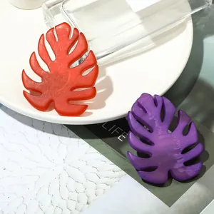 Artistic monstera leaf acrylic brooches in marble orange and purple on a stylist magazine