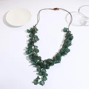 Collier artisanal avec feuilles en résine vert foncé et cordon marron sur fond blanc
