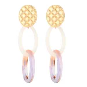Détail de boucles d'oreilles en acrylique avec texture matelassée dorée et motif marbré
