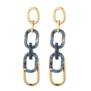 Détail de longues boucles d'oreilles dorées avec pendentif en acrylique marbré bleu