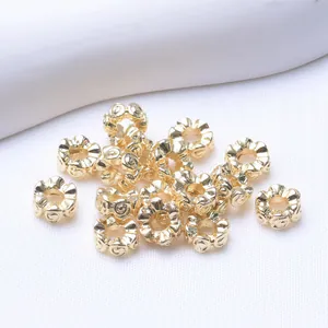 Goldene Abstandsperlen mit Blumenrelief für DIY-Schmuck auf weißem Textilhintergrund