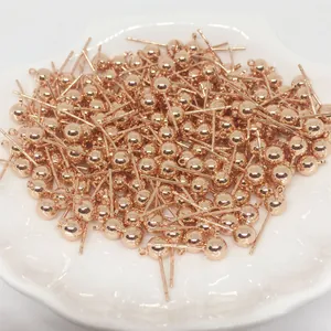 Gros plan de clous d'oreilles boules en or rose en vrac sur un plateau en céramique