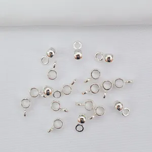 Polierte silberne Anhängerösen und Zwischenperlen für DIY-Schmuck auf weißem Textilhintergrund