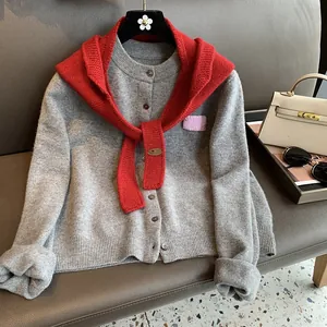 Detail of red chunky knit shawl with brown leather logo tag over gray cardigan