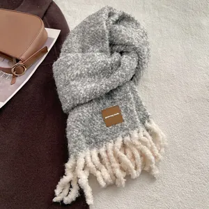 Détail d'une écharpe en laine mélangée avec franges blanches et étiquette en cuir