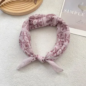 Détail d'un foulard en coton rose clair avec motif de feuilles rouges sur fond blanc