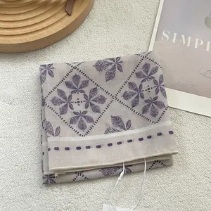 Détail d'un foulard carré bleu-gris avec motifs de feuilles mauves et bordure losange