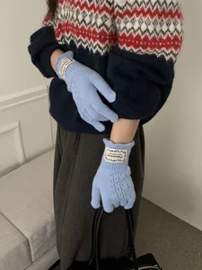 Close-up of light blue cable knit gloves with hollow patterns and branded wrist label