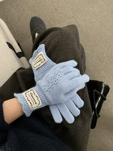 Close-up of light blue knit gloves with lace cut-outs and ruffled cuffs with fabric label