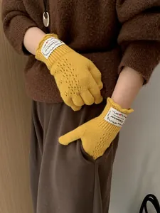 Detail of yellow knit glove featuring hollow diamond pattern and decorative logo patch
