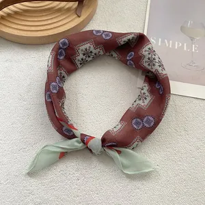 Detail eines Seidenschals mit Blumenmuster und grünen Chiffon-Enden auf weichem Teppich