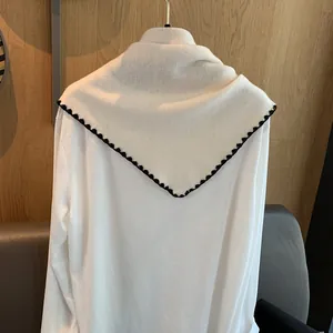 Gros plan sur un châle en laine blanche avec bordure crochetée noire sur un cintre