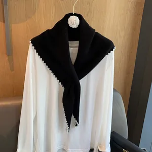 Détail du châle en laine noire avec bordures en crochet blanc sur une chemise blanche