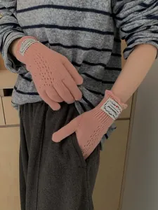 Close-up of pink knit gloves featuring delicate hollow lace patterns and retro cloth tags