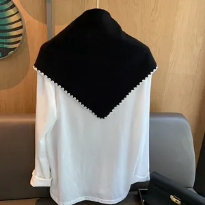 Détail d'un châle en laine noir avec bordure festonnée blanche sur chemise blanche