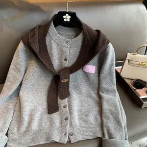 Detail of grey knitted cardigan and dark brown shawl with leather logo tag