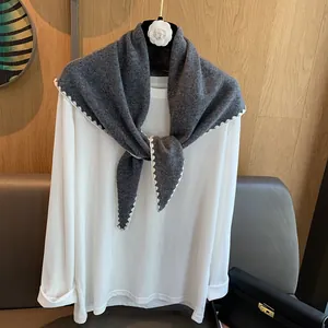 Détail d'un châle en laine gris foncé avec bordure festonnée sur un haut blanc simple
