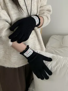 Close-up of black knitted gloves with decorative label and elastic cuff on a model