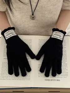 Close-up of black knitted gloves with scalloped cuffs and a stylish white woven label