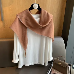 Detail eines braunen Baumwoll-Leinen-Schals mit Quasten über einem weißen Langarmshirt