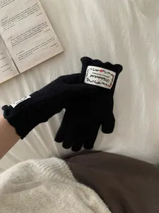 Close-up of black knitted gloves with white floral label and wavy ruffles on cuffs