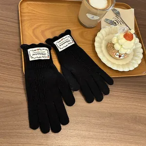 Close-up of black knit gloves featuring a vintage white label on a cozy wooden table