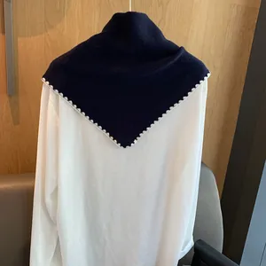 Détail d'un châle en tricot bleu marine avec bordure en dentelle sur un haut blanc à manches